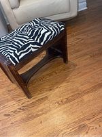 Side angled view of the stool showing zebra print upholstery and wooden legs with wear and scratches