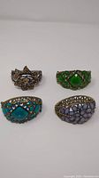 Group photo of four gemmed cuffed bracelets including bow design, green gem, turquoise centerpiece, and lavender petal bracelet