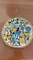 Top down view of a round ceramic plate showing detailed colorful bird and flowers with gold rim