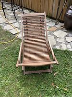 Front view of wooden folding chaise lounge chair placed on grass and stone patio.