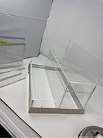 Photo showing large lucite organizer with metal base frame, clear and rectangular, placed on white surface with a backdrop.