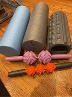 Five muscle release tools including three foam rollers and two manual spike massagers arranged on the floor.