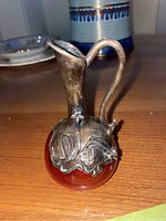 Front angled view showing detailed silver neck and handle, floral motifs, and cranberry glass base.