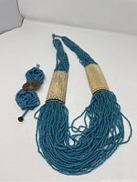 Turquoise multi-strand beaded necklace with two large curved metal accent bars and matching bracelet with metal button clasp arranged against a white background.