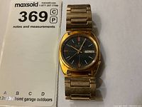 Full view of Bulova Accutron watch showing gold-tone case, black dial, and metal expansion bracelet.