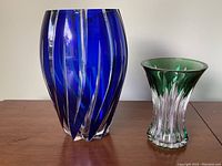 Pair of vases on wooden surface showing cobalt blue vase with vertical cut patterns and green vase with flared rim and vertical clear cuts