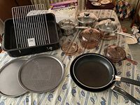 Full lot showing roasting pan, glass saucepans, copper-colored pots, frying pans, and baking pans on a table.