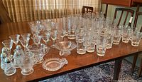 Full view of Hughes Cornflower glassware set on a wooden table in a dining room including various stemmed glasses, tumblers, condiment sets, and small dishes.