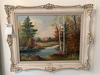 Full view of the framed landscape oil painting showing river, trees, and autumn foliage.
