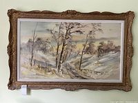 Full view of large framed vintage oil painting of a winter landscape showing snowy hills, road, trees, and distant cabin.