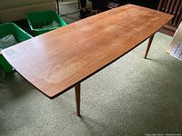 Full view of rectangular teak coffee table with tapered legs on carpeted floor, showing surface wear and discoloration.