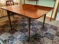 Three-quarter front view of walnut dining table assembled with leaves inserted, showing tapered legs and wood grain top.