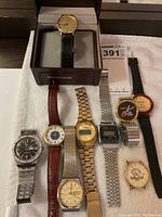 Full view of eight men's watches including the Wittnauer in original box and several analog and digital watches arranged on white cloth.