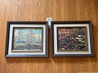 Pair of framed landscape prints attributed to Group of Seven artists, hung on a wooden floor background. Both prints feature nature scenes with distinct color palettes and wooden frames with cream-colored liners.