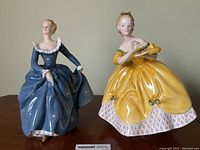 Both Royal Doulton figurines displayed side-by-side on a wooden surface against a neutral background.