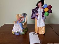 Photo showing both Royal Doulton figurines, "Sweet Dreams" and "Balloon Lady", on a wooden surface
