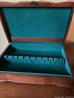 Open wood flatware case showing green felt lining and slots for holding flatware pieces.