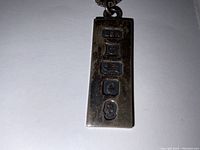 Close-up photo of the sterling silver ingot pendant showing British hallmarks stamped on one side.