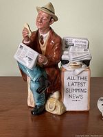 Front view of ceramic figurine holding hotdog and newspaper with headline about slimming news.
