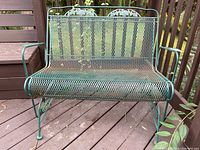 Front view of the green wrought iron two-seater bench with mesh seating and backrest, showing the floral decorative round motifs on top backrest.