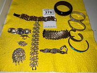 Overview of lot showing various bracelets, brooch, and earrings arranged on a yellow cloth.