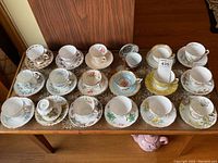 Full view of 20 vintage bone china cups and saucers arranged in rows on a wooden table.
