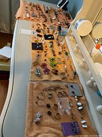 Wide view of all vintage earrings laid out on three brown towels showing the entire lot and variety of styles and colors including black, white, green, metal, and enamel portions