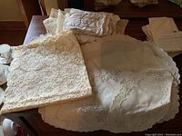 Lot of vintage linens spread on table showing handmade lace doilies, embroidered handkerchiefs, and damask tablecloth with scalloped edges and embroidery