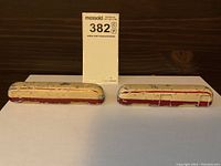 Two vintage TTC heavy cast street car models displayed on white paper with a lot tag, showing front and side views with worn cream and maroon paint