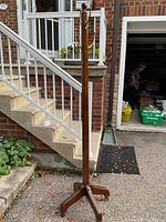 Full height view of the wooden standing coat rack placed outdoors near stairs and a house entrance.