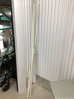 Four white curtain rods standing vertically against a wall, showing entire length and end caps.