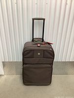 Brown Delsey softside luggage with extendable handle and front zippered compartments, positioned front-facing to show full luggage.