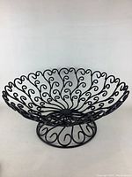 Black metal decorative fruit bowl viewed from front with detailed scrollwork pattern and pedestal base