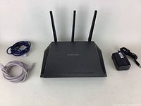 Netgear Nighthawk router with three antennas, power adapter, and two Ethernet cables shown on white background.