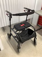 Angled side view of the Nexus folding walker showing the padded seat, storage basket, four wheels, and padded handles.
