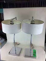 Pair of chrome table lamps with white shades photographed together from multiple angles on a white surface with a black and silver background.