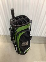 Front-right side view of Ping golf bag showing open top and umbrella handle, standing upright on concrete floor.