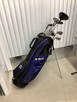 Wilson stand bag with retractable legs holding Callaway clubs against white corrugated wall