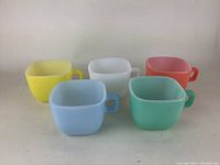Front view of 5 vintage square coffee mugs in yellow, white, coral pink, light blue, and mint green showing color and handle design