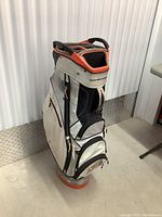 Side view of Sun Mountain golf bag showing its beige and black fabric with orange accents and multiple zippered compartments.