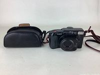 Canon 35mm film camera with carrying case on left, camera showing front with lens, built-in flash, and attached strap visible