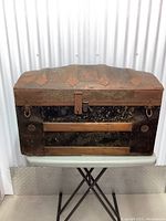 Front view of vintage treasure trunk showing domed lid with metal straps, wood slats, and metal hardware with patina.