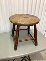 Vintage rustic wooden stool with round top and four legs on light gray table against white backdrop.