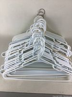 Stack of approximately 30 white plastic clothing hangers with two metal hooks on top