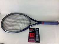 Wilson tennis racket with blue grip and replacement grip packet shown alongside