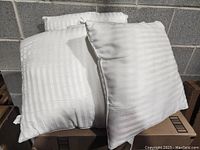 Four new white throw pillow inserts with checkered stripe pattern stacked outdoors against concrete blocks.