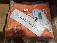 Packaged orange-red sun shade sail with white rope and metal attachment ring visible, labeled 6.5ft x 10ft size.