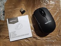 Wireless mouse with nano receiver and user manual on a brown surface.