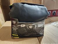 Black perforated leather-like seat covers in original packaging with partial box visible showing brand and product details.