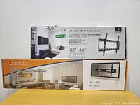 Photo showing the two TV wall mount boxes stacked, one GTECH and one IKROSS, indicating sizes and tilt mounts.